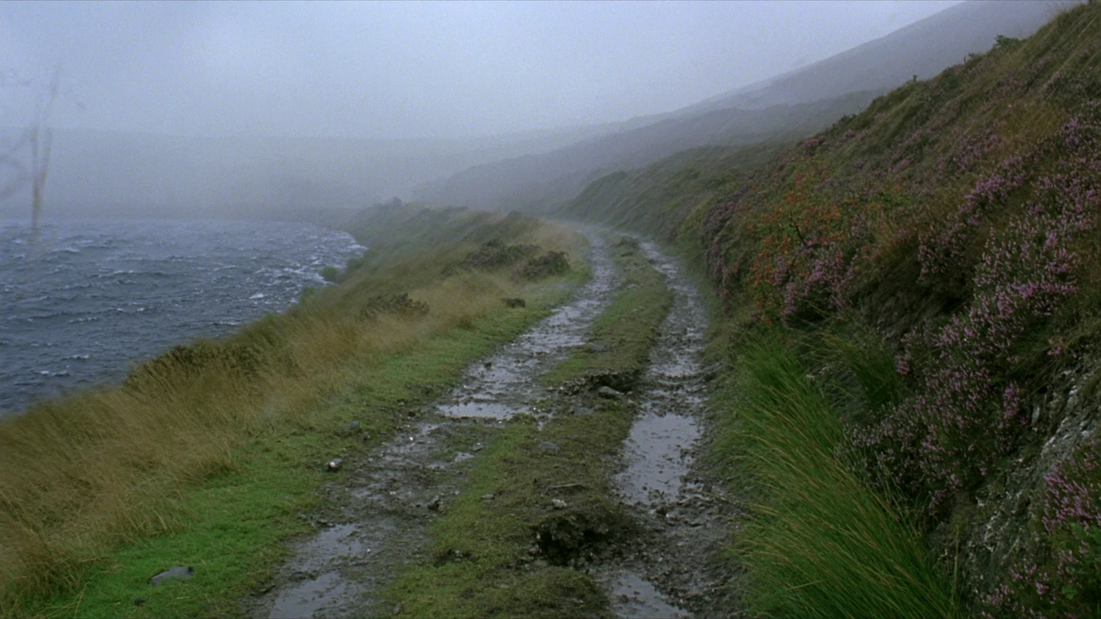 Rain sweeps across the narrow Highland path above the loch