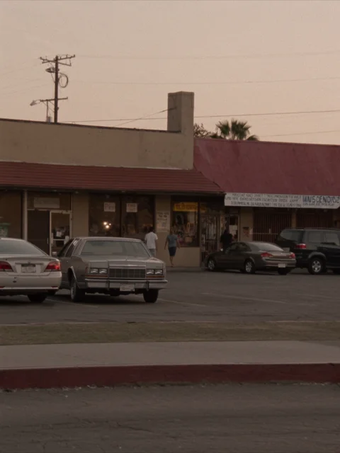A modest Bakersfield strip mall with a burgundy awning, parked cars and customers outside.